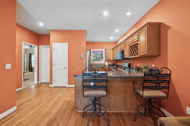 kitchen featuring dark countertops, brown cabinets, a peninsula, light wood finished floors, and stainless steel appliances