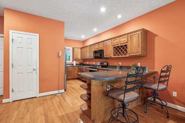 kitchen with dark countertops, baseboards, a kitchen breakfast bar, light wood finished floors, and stainless steel appliances