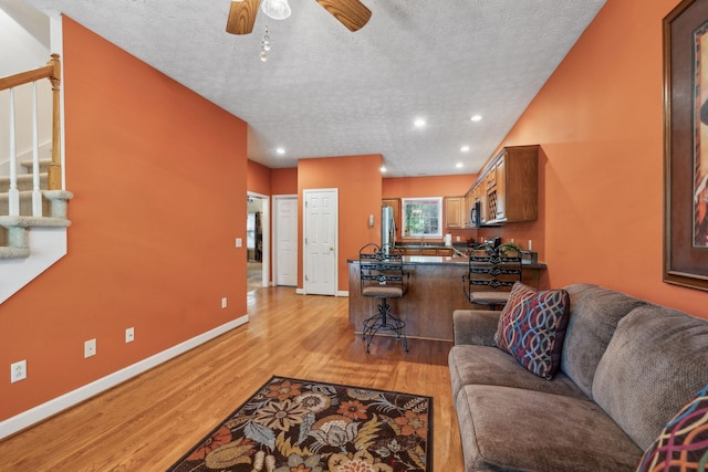 living room with baseboards, ceiling fan, recessed lighting, a textured ceiling, and light wood-style flooring
