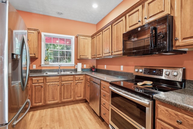 kitchen with a sink, dark countertops, light wood-style floors, and stainless steel appliances
