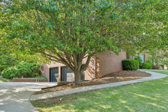 view of property exterior with a lawn, brick siding, an attached garage, and driveway