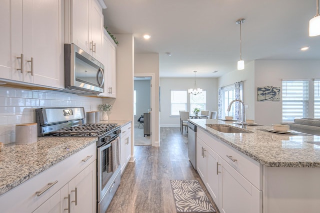 kitchen with decorative backsplash, light wood-style floors, an island with sink, a sink, and stainless steel appliances