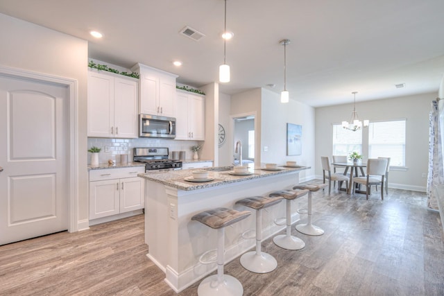 kitchen featuring white cabinets, appliances with stainless steel finishes, light wood-style flooring, backsplash, and visible vents