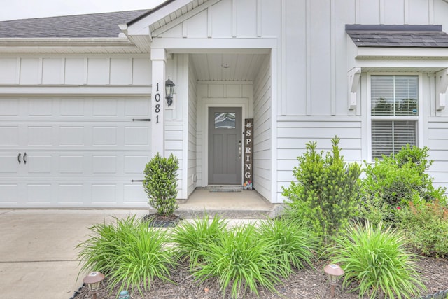 doorway to property featuring roof with shingles, board and batten siding, concrete driveway, and a garage