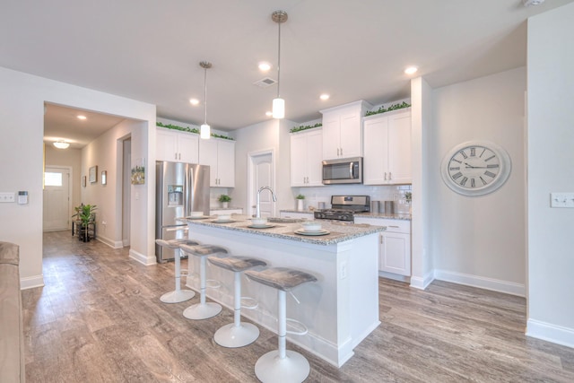 kitchen featuring a kitchen breakfast bar, a kitchen island with sink, white cabinets, light wood finished floors, and stainless steel appliances