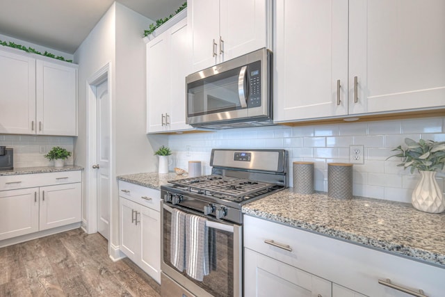 kitchen featuring light stone countertops, appliances with stainless steel finishes, light wood-style floors, white cabinetry, and backsplash