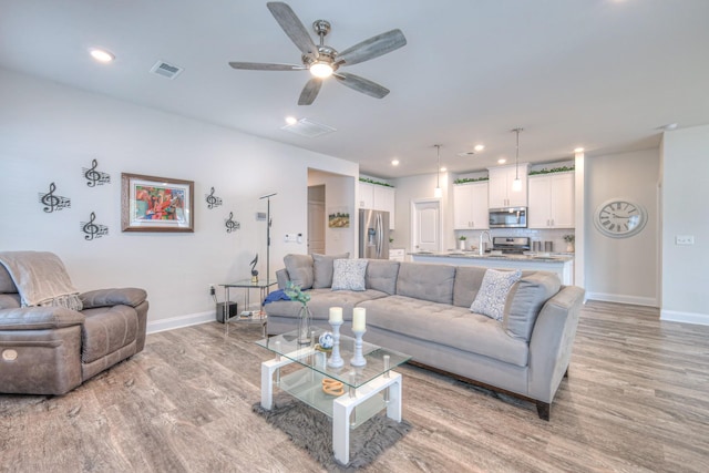 living area featuring baseboards, a ceiling fan, light wood-style flooring, and visible vents