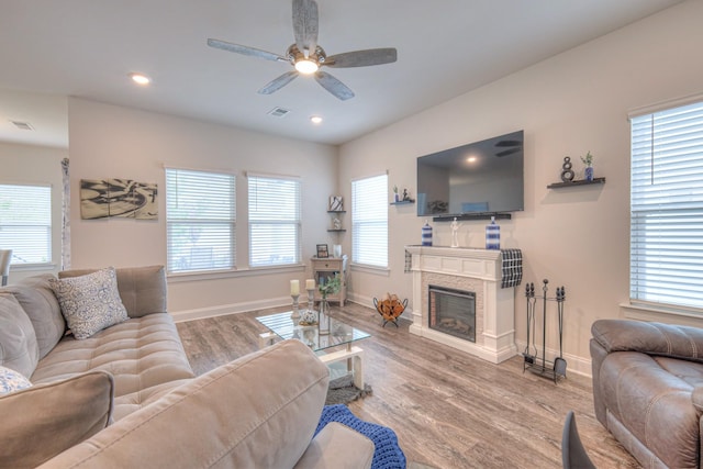 living room with a ceiling fan, visible vents, wood finished floors, baseboards, and a glass covered fireplace