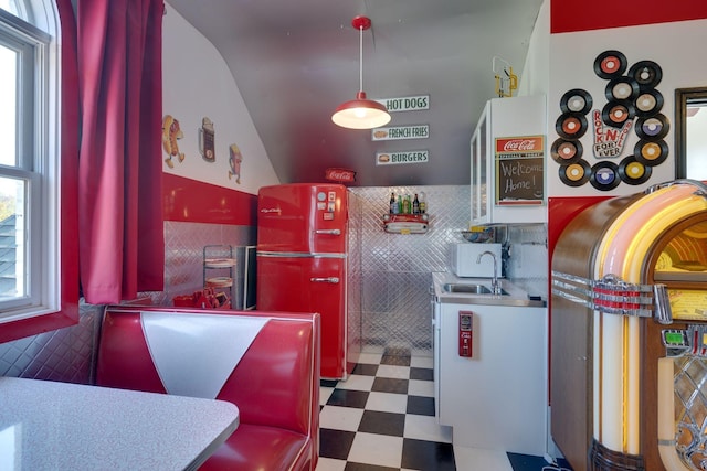 kitchen featuring a sink, tile patterned floors, vaulted ceiling, and tile walls