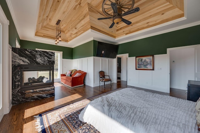 bedroom featuring wood ceiling, wood finished floors, a raised ceiling, ornamental molding, and a decorative wall