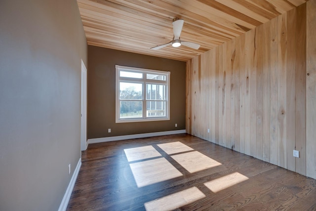 unfurnished room with baseboards, ceiling fan, wood walls, and wood finished floors