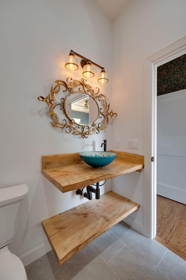 half bath with toilet, baseboards, a sink, and tile patterned floors