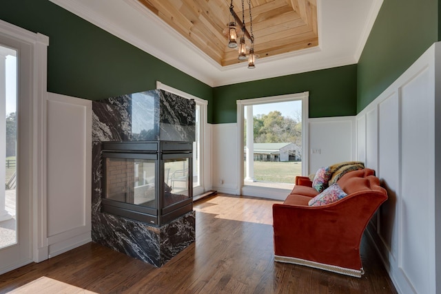 living area with wood finished floors, ornamental molding, a raised ceiling, and a decorative wall