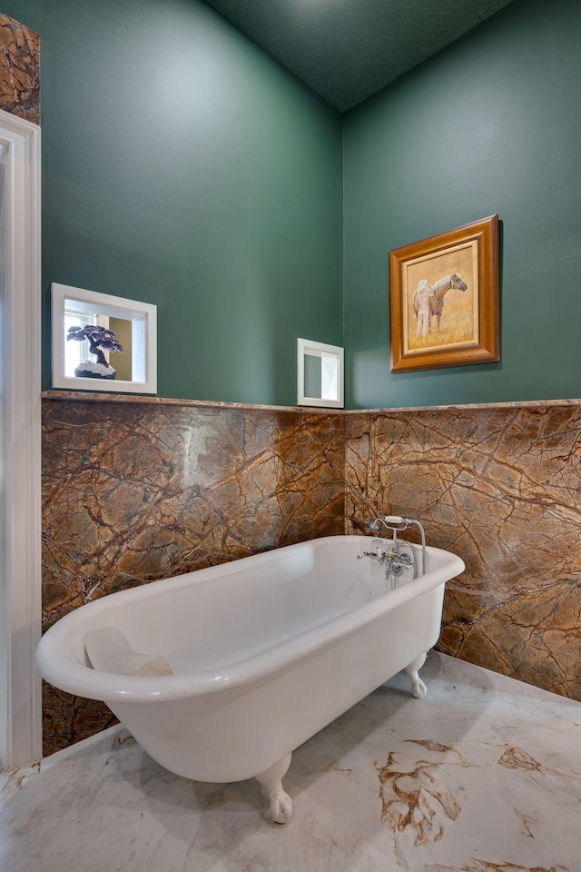 bathroom with a high ceiling, marble finish floor, a wainscoted wall, a freestanding tub, and tile walls