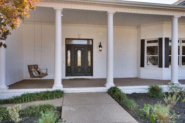 property entrance with a porch and brick siding
