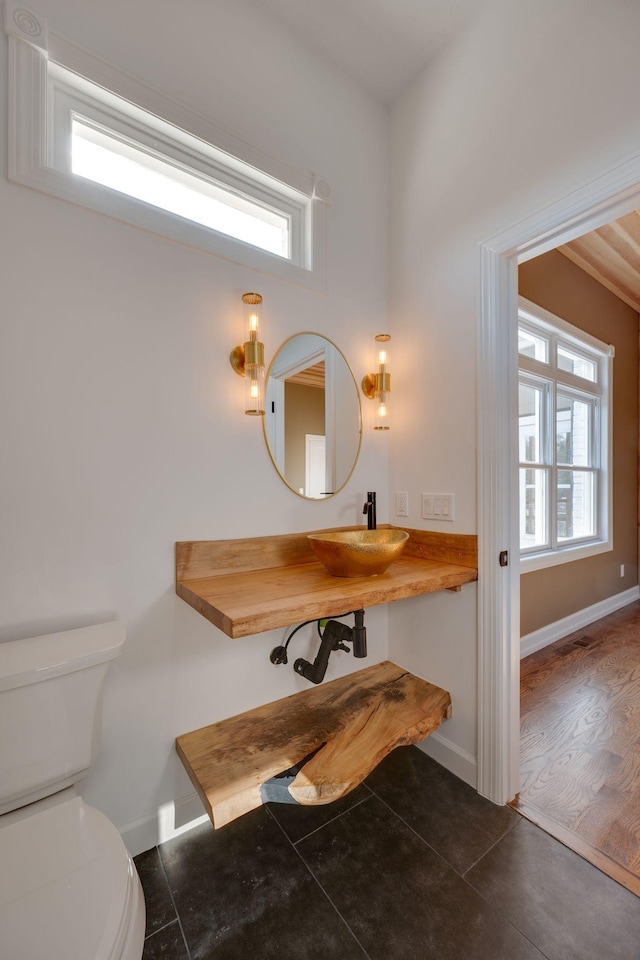 bathroom with a sink, baseboards, toilet, and a healthy amount of sunlight