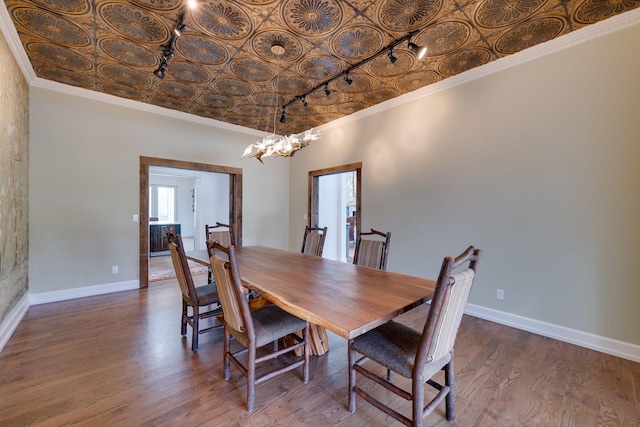 dining space featuring crown molding, an inviting chandelier, wood finished floors, baseboards, and an ornate ceiling