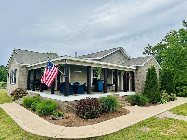 exterior space featuring covered porch, roof with shingles, brick siding, and a lawn