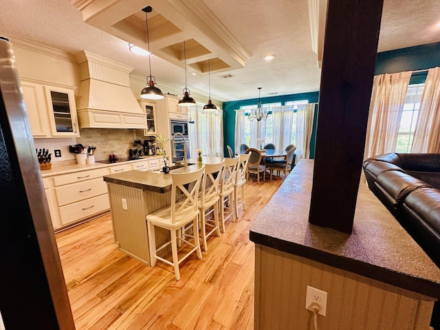 kitchen featuring a notable chandelier, custom exhaust hood, a kitchen bar, crown molding, and light wood-style floors