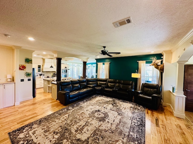 living area featuring a textured ceiling, ornate columns, a ceiling fan, and visible vents