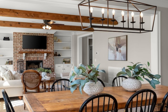 dining room featuring a brick fireplace, a ceiling fan, beamed ceiling, and built in shelves