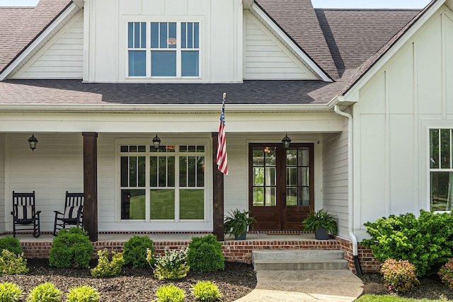 view of exterior entry featuring a porch, a shingled roof, and board and batten siding