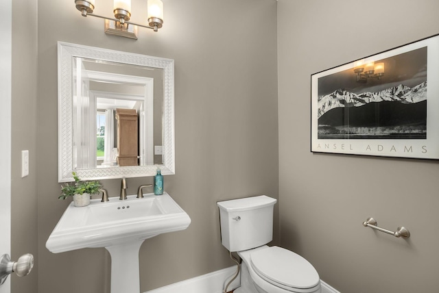 half bathroom featuring toilet, baseboards, a chandelier, and a sink