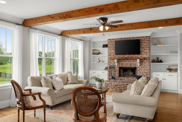 living area with built in features, beam ceiling, a fireplace, light wood-style floors, and a ceiling fan