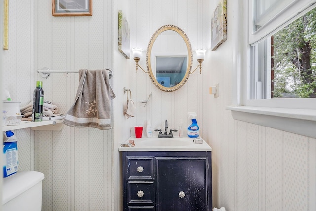 half bathroom with toilet, wallpapered walls, and vanity