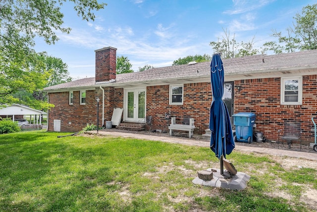 back of house featuring brick siding, french doors, entry steps, a chimney, and a lawn