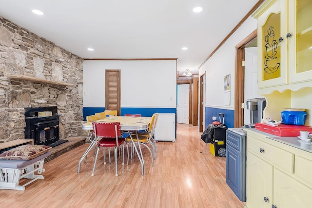 dining area with crown molding, light wood-style floors, a wainscoted wall, and a fireplace