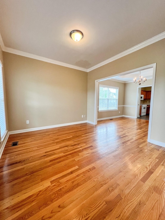 spare room with crown molding, a notable chandelier, light wood finished floors, baseboards, and visible vents