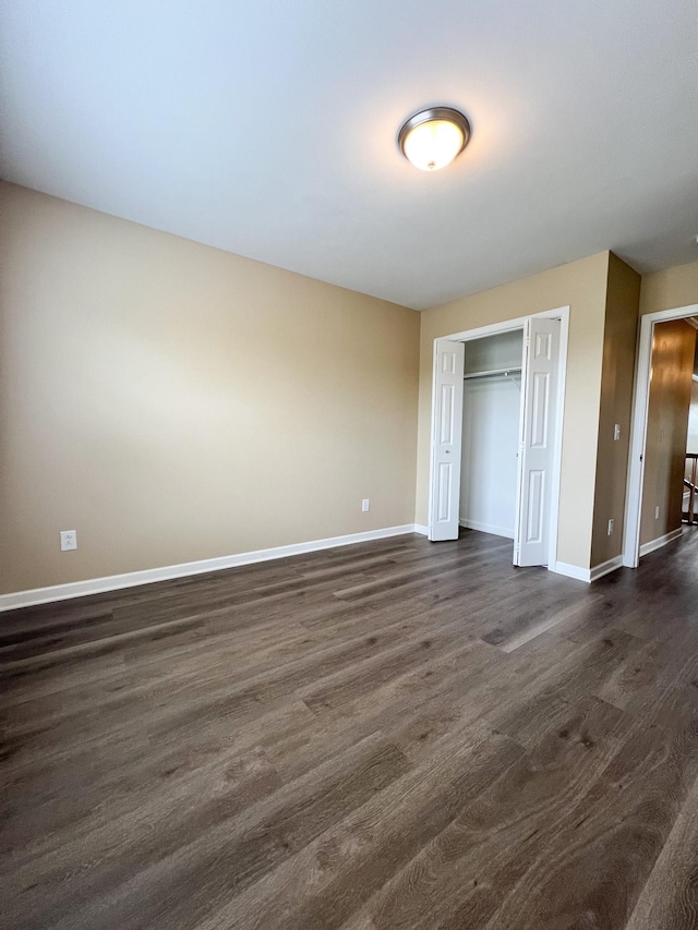 unfurnished bedroom with baseboards, dark wood-type flooring, and a closet