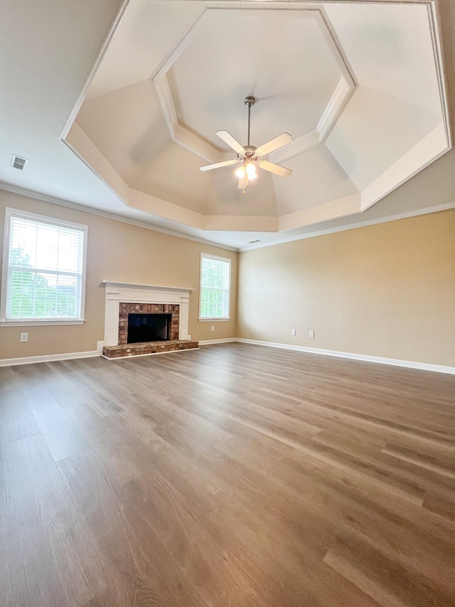 unfurnished living room with a ceiling fan, visible vents, a brick fireplace, wood finished floors, and a raised ceiling