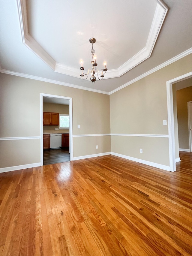 unfurnished room featuring an inviting chandelier, light wood finished floors, crown molding, and a tray ceiling