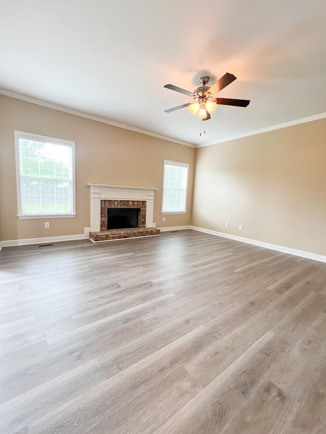 unfurnished living room featuring a ceiling fan, crown molding, a brick fireplace, wood finished floors, and baseboards