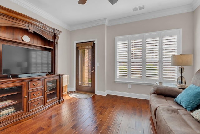 living area featuring a ceiling fan, visible vents, baseboards, ornamental molding, and dark wood-type flooring