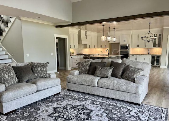 living area with wine cooler, baseboards, a chandelier, light wood-style floors, and stairs