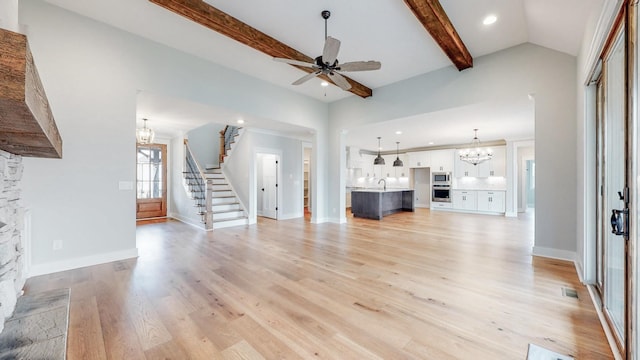 unfurnished living room with lofted ceiling with beams, stairway, a sink, light wood finished floors, and ceiling fan with notable chandelier