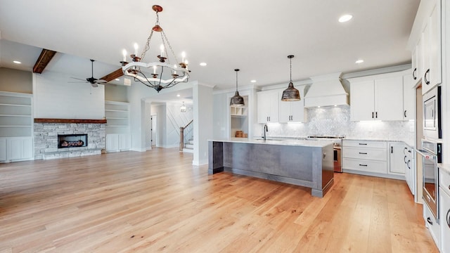 kitchen featuring an island with sink, ceiling fan with notable chandelier, stainless steel appliances, tasteful backsplash, and custom exhaust hood