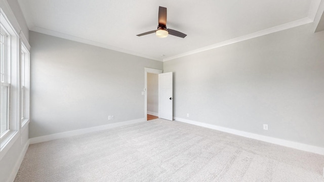 carpeted empty room with crown molding, a ceiling fan, and baseboards