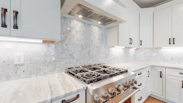 kitchen with high end stainless steel range, premium range hood, white cabinetry, light stone counters, and backsplash