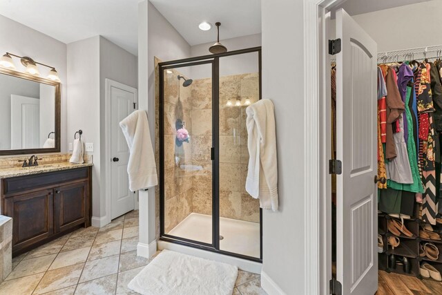 bathroom featuring vanity, baseboards, a stall shower, and a spacious closet