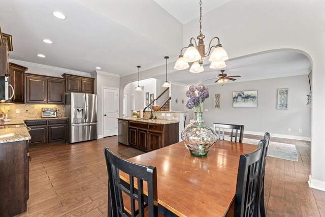 dining space with ornamental molding, dark wood-type flooring, recessed lighting, arched walkways, and ceiling fan with notable chandelier