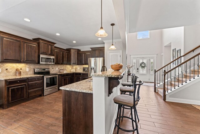 kitchen featuring crown molding, stainless steel appliances, wood finished floors, and dark brown cabinets