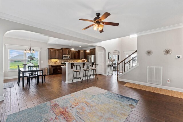 living area featuring arched walkways, dark wood finished floors, ceiling fan with notable chandelier, baseboards, and visible vents