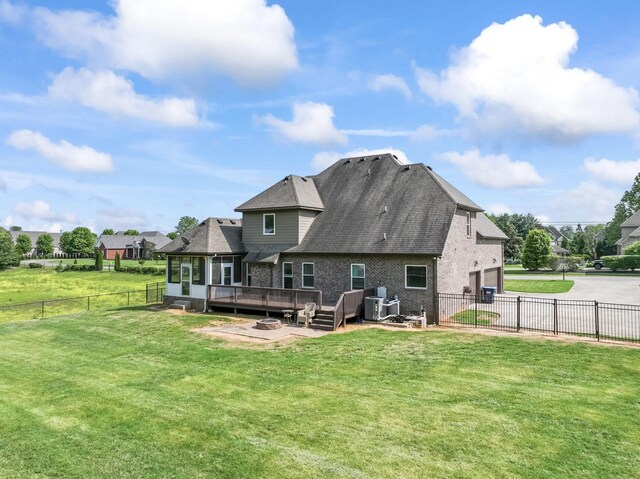 back of property featuring driveway, a deck, brick siding, a fenced backyard, and a yard