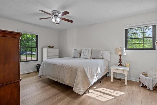 bedroom with light wood-style floors, a ceiling fan, and baseboards