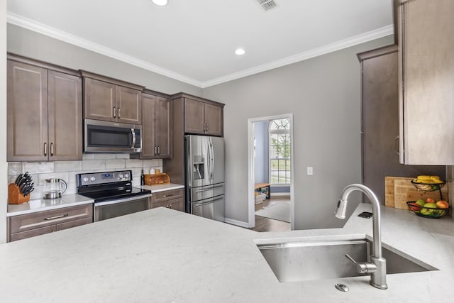 kitchen featuring crown molding, light stone countertops, a sink, appliances with stainless steel finishes, and backsplash
