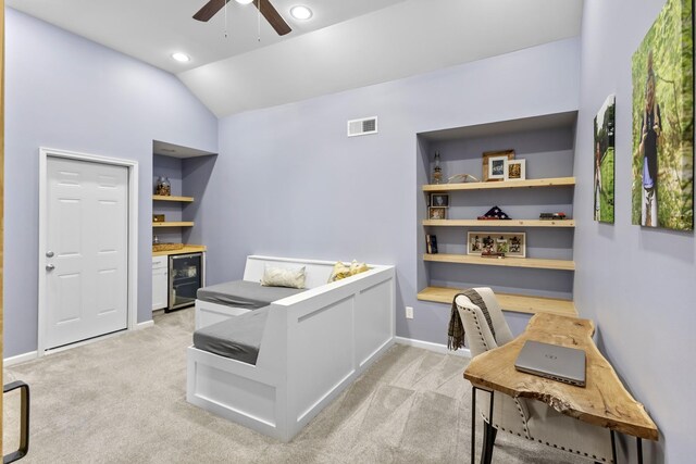 home office with ceiling fan, light colored carpet, visible vents, vaulted ceiling, and beverage cooler